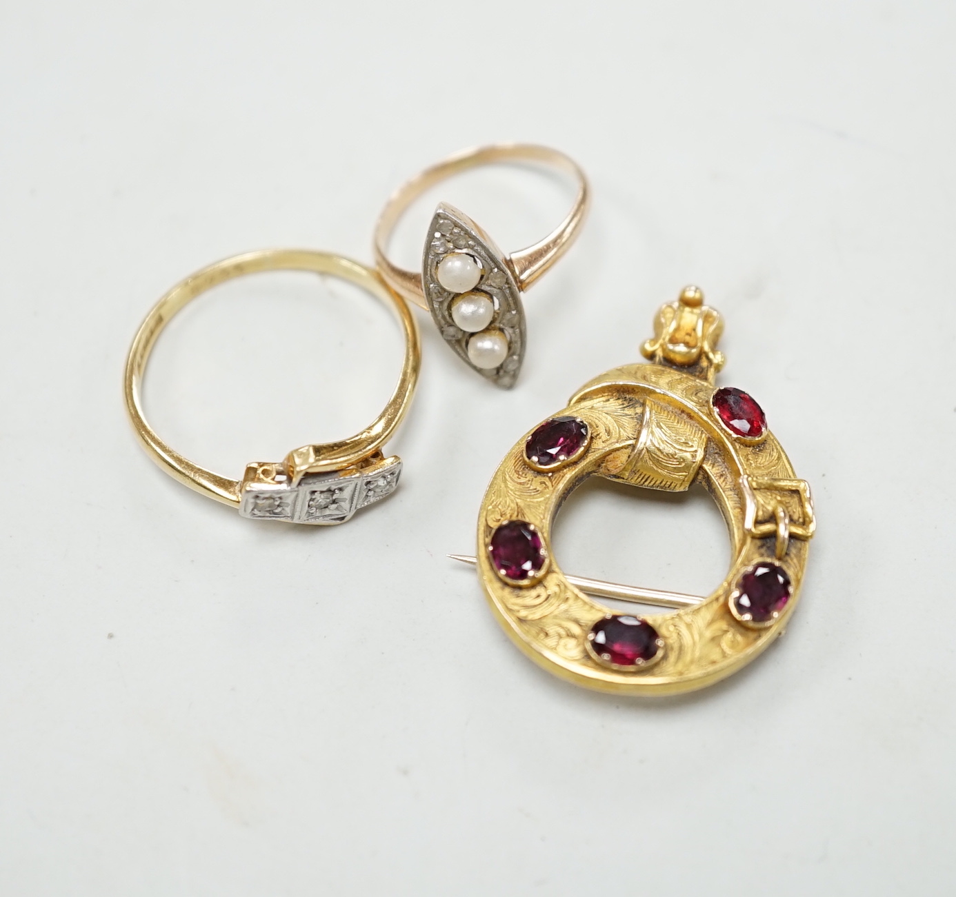 An 18c, pt and illusion set three stone diamond crossover ring, size T, a 585, three stone seed pearl and diamond chip set marquise shaped ring and a Victorian yellow metal and garnet set open work 'belt with buckle' bro